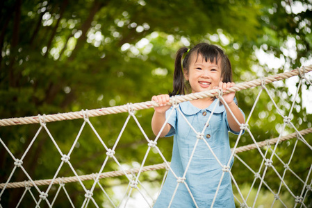在炎热的夏日, 快乐的小女孩在冒险公园的绳索桥上攀登。儿童暑期活动