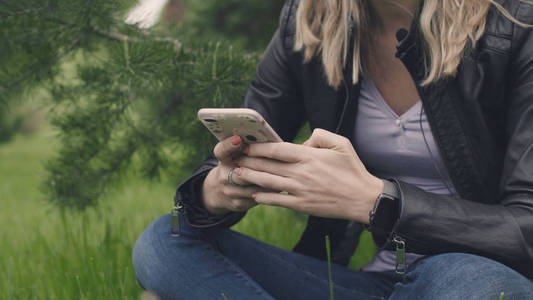 女人坐在草地上, 手里拿着电话, 一只聪明的手表。股票。日常生活中的技术概念