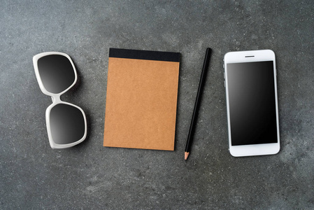 白色智能手机, 太阳镜和笔记本上的灰色石材背景
