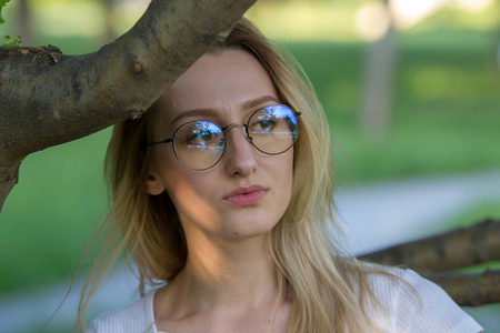 在公园的树枝上的眼镜年轻漂亮的女人的肖像