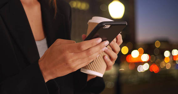 新发短信女人手发短信与手机和咖啡杯在晚上照片