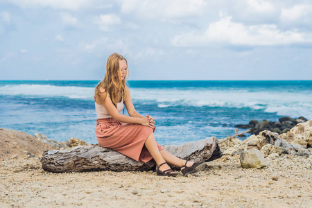 年轻的女性旅行者休息在惊人的梅拉斯蒂海滩与绿松石水的岩石, 巴厘岛, 印度尼西亚