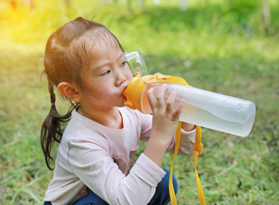 把小女孩从公园里的瓶子里喝水.人像户外照片