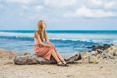 年轻的女性旅行者休息在惊人的梅拉斯蒂海滩与绿松石水的岩石, 巴厘岛, 印度尼西亚