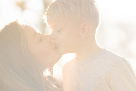 快乐的孩子男孩亲吻与妈妈在公园里玩太阳光色调
