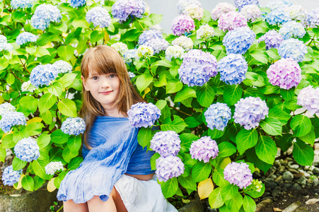 夏天的可爱的小女孩坐在中间的花朵的肖像
