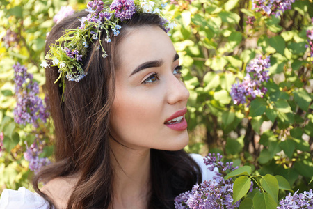 阳光明媚的春天, 美丽的年轻女子戴着花环靠近盛开的灌木