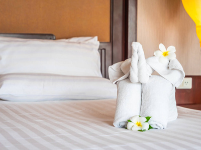 白色象毛巾和舒适的枕头在床装饰在旅馆卧室内部