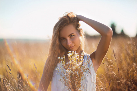 有吸引力的年轻女子站在草地上无袖牛仔裤太阳礼服递给她的长发
