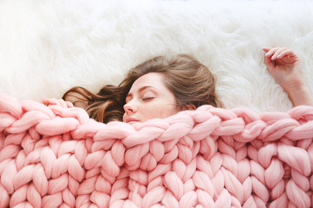 长棕色头发的年轻妇女睡在温暖的针织桃颜色投掷毯子之下