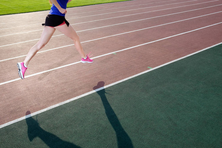 运动。穿着粉红色运动鞋的运动年轻女子奔跑在跑道体育场上。概念运行