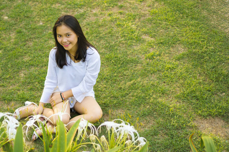 愉快的微笑年轻的亚洲十几岁的女孩坐在公园的草地上