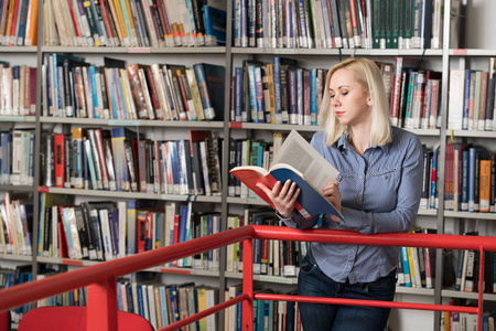 在图书馆漂亮的女学生与书工作在高中大学图书馆浅景深
