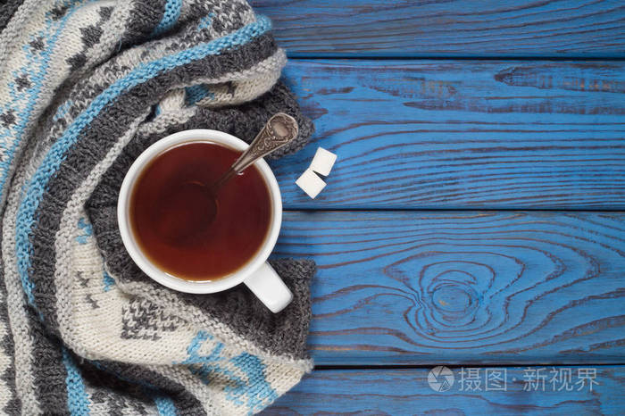 蓝色木桌背景上的一杯茶和一条针织围巾