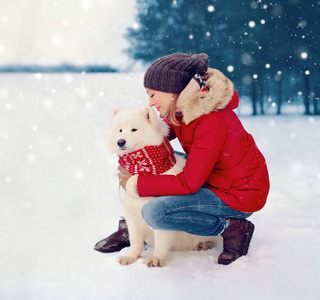 愉快的妇女主人拥抱白色萨摩耶狗在冬季圣诞节飞行雪花雪背景
