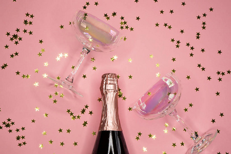 香槟酒瓶与眼镜和金色的五彩纸屑在粉红色的背景