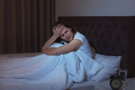 晚上坐在床上的可怕头疼的年轻妇女