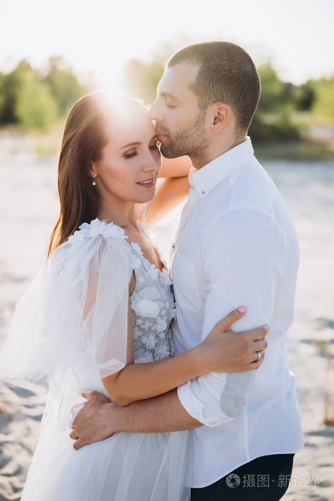 美丽幸福的情侣拥抱在海滩上与背部灯