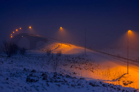 冬季挪威。在傍晚和降雪的峡湾与灯笼的桥梁