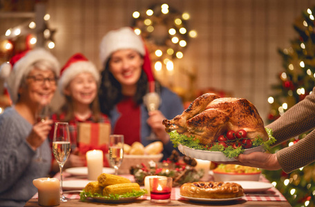 圣诞快乐幸福的家庭正在家里吃晚饭。庆祝节日和团结在树附近