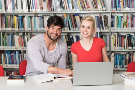 在图书馆英俊的两个大学生与笔记本电脑和书籍工作在一个高中大学图书馆