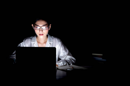 在她家办公室工作到很晚的女人。美丽的亚洲妇女工作在她的电脑, 全集中, 戴眼镜。现代全球互联业务理念