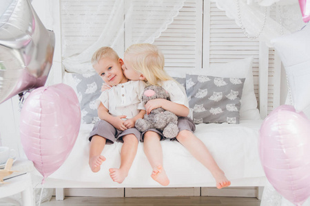 小妹妹和弟弟坐在床上的衣服。假日与气球。色调