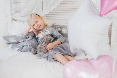 穿着漂亮衣服的快乐女孩躺在床上, 一头长毛绒猫。用气球庆祝节日。色调