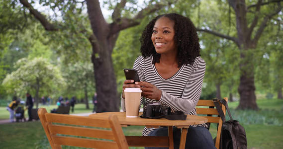 在城市公园里, 坐在桌旁拿着电话的漂亮黑人妇女的肖像