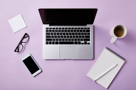 在粉红色桌面上使用笔记本电脑和智能手机的工作场所的顶级视图