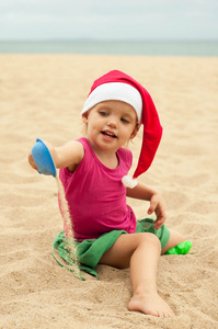 可爱的女孩在玩沙的圣诞老人的帽子