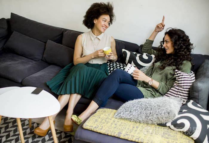 两个多种族的年轻妇女在客厅里聊天喝咖啡