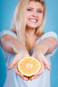 女人持有一半黄色葡萄柚柑橘果实在手中，在蓝色的小女孩微笑着。健康的食物，饮食概念