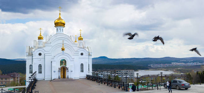 萨罗夫圣天使寺在 Zlatoust 的阴天。基督教教会。鸟儿飞得很近。远处的河水