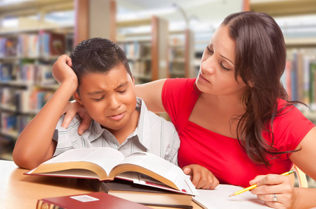 不安的西班牙裔年轻男孩和 Famle 成人在图书馆学习