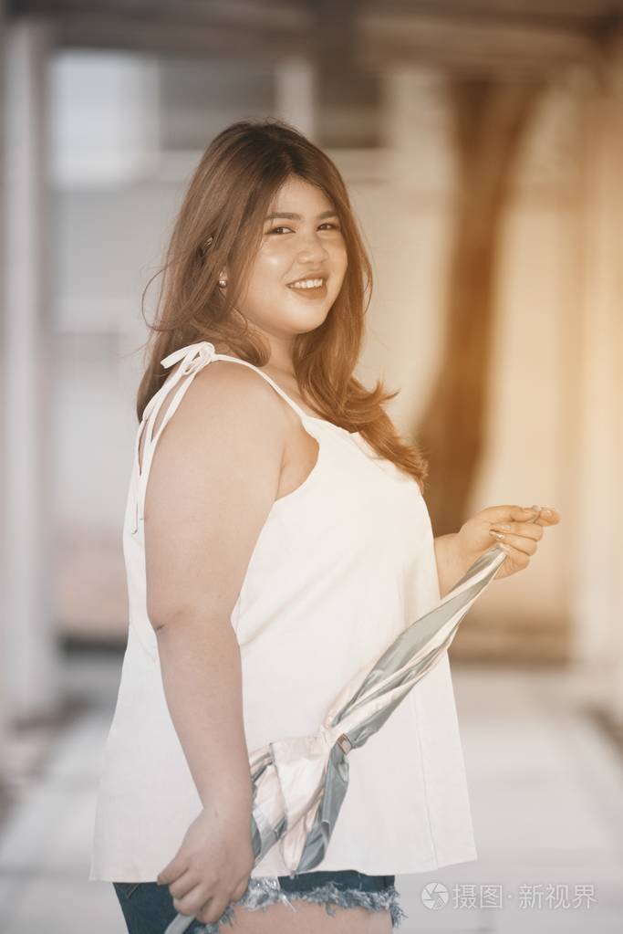 亚洲漂亮的笑脸脸胖女人姿势站立, 并持有雨伞在人行道上