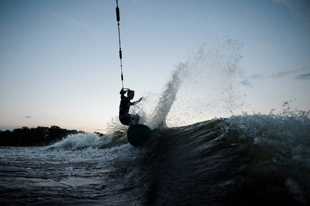年轻的 wakesurfer 穿着泳装骑在蓝色河波浪与飞溅在夏天晚上