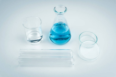实验室设备。白色桌上的蓝色液体烧瓶透明液体烧杯试管和培养皿