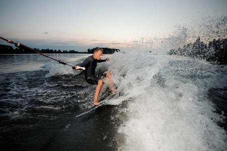 活跃的 wakesurfer 穿着泳装骑在蓝色河波浪与飞溅在夏天晚上