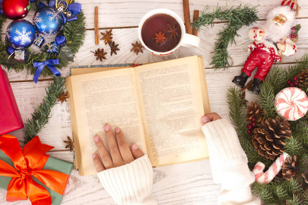 圣诞节背景。女孩阅读书籍和喝茶附近的礼品盒和松树冷杉。新年心情