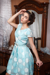 美丽的年轻女孩在蓝色礼服在镜子附近在橡木框架