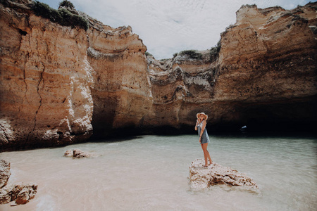 在悬崖海滩上的海洋水中站在小岩石上的年轻美女妇女