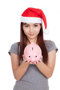 红色的圣诞帽的亚洲女孩举行一个粉红色的存钱罐