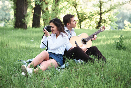 年轻夫妇在森林里漫步, 弹着吉他, 拍着老相机上的照片, 夏日的自然, 灿烂的阳光, 阴影和绿叶, 浪漫的情怀。