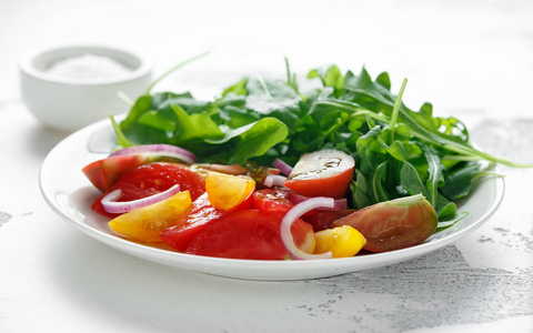 彩色西红柿沙拉与野生火箭在一个白色的盘子。健康食品