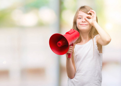 年轻的金发小拿着扩音器与快乐的脸微笑着做 ok 标志用手在眼睛看通过