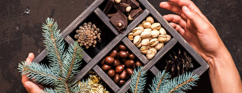 长横幅。黑暗背景下的圣诞作文。装饰木箱与坚果, 糖果在金色包装, 一块巧克力, 锥和几个世纪的云杉。手捧礼物