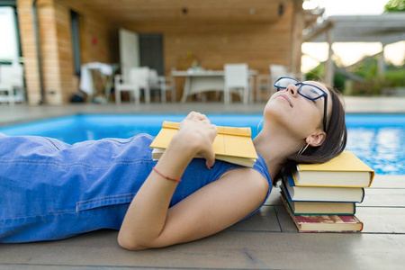 小女孩戴着眼镜, 在水池边上堆着书, 看书。教育暑期知识
