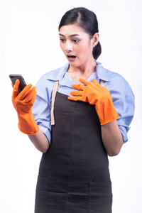 房屋清洁服务妇女查出的白色。亚洲年轻妇女与手套, 使用手机, 惊喜的姿势。网上房屋清洁服务概念