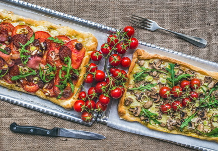 与新鲜的芝麻菜和樱桃西红柿在银屏上的两个方形比萨饼